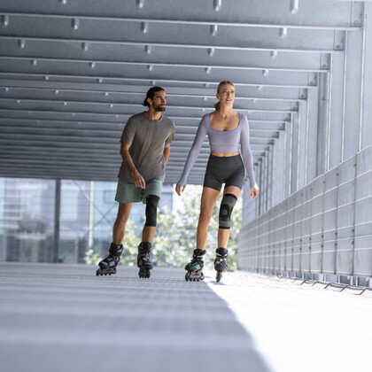 A man and a woman wearing knee braces are rollerblading in a garage.