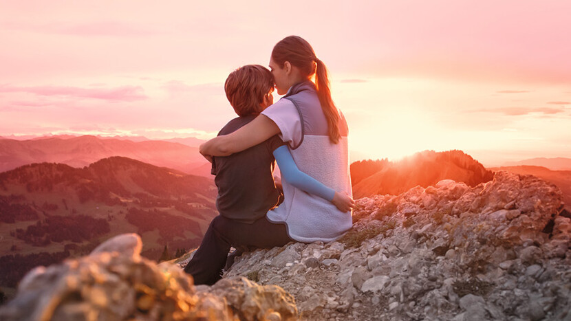 Traitement des cicatrices Une mère est assise avec son enfant au sommet d'une montagne. L'enfant porte une manchette de compression.