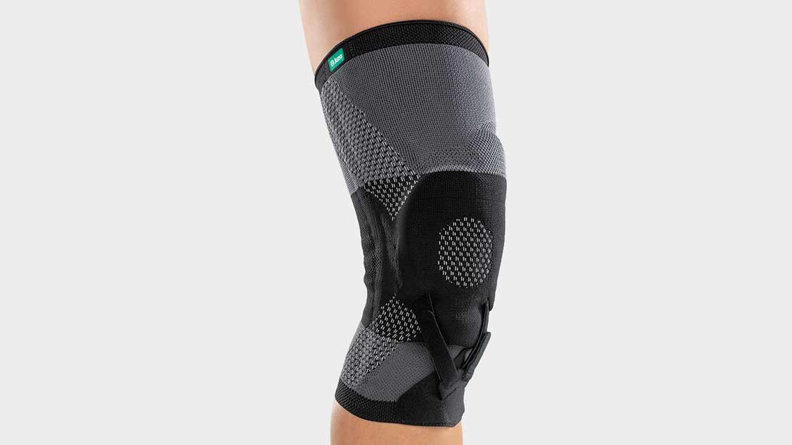 A woman is sitting on the floor in the gym. She is wearing a knee brace