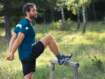 Ein Mann in Sportklamotten im Wald dehnt sich an einem Holzbalken