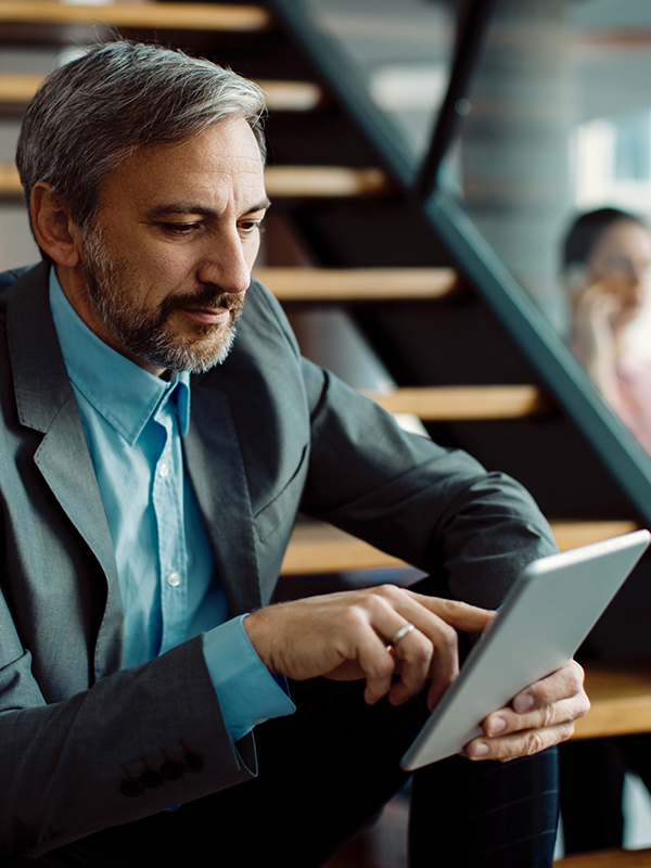 A man in a suit is sitting on a flight of stairs, tapping away on a tablet