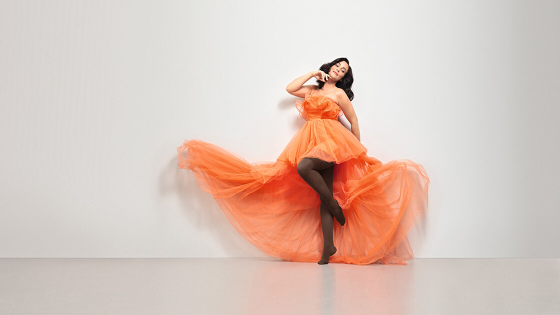 A woman in an orange dress. She is wearing Juzo Inspiration brown tights.
