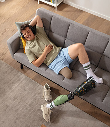 Allongé sur le canapé sans son orthèse, un jeune homme porte le bas-moignon de compression Juzo Classic Seamless breveté
