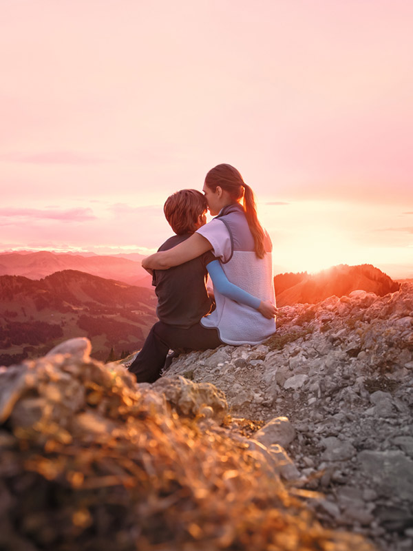 A mother is sitting on a mountain peak with her child. The child is wearing a compression sleeve. A mother is sitting on a mountain peak with her child. The child is wearing a compression sleeve.